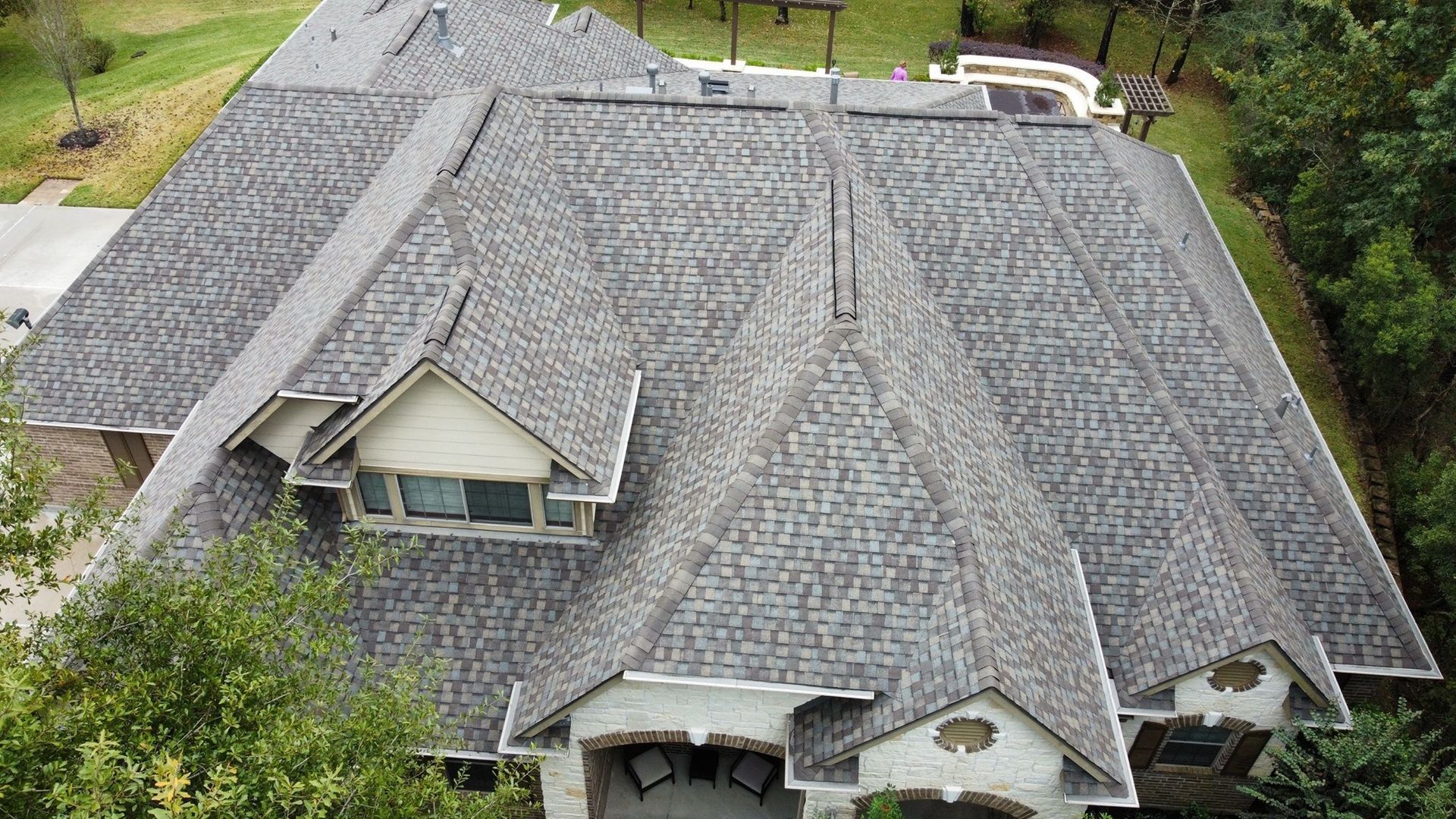 Gray asphalt shingle roof on a multi-gabled house surrounded by trees.