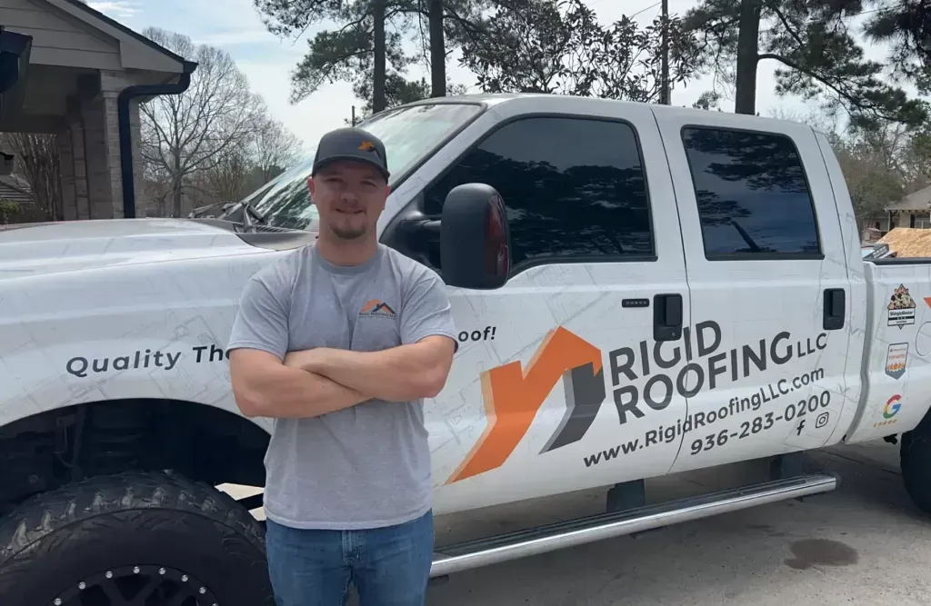 Man in front of a white Rigid Roofing truck, arms crossed. The truck has company logo and contact info on the side.