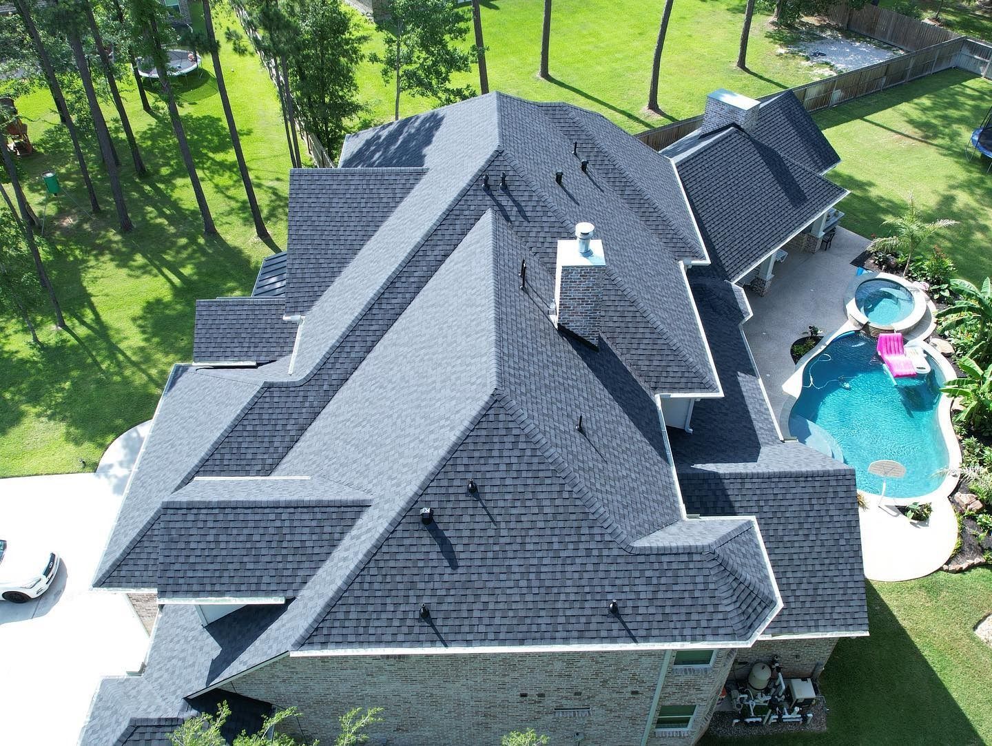 Overhead view of a house with a complex, dark roof and a pool in the backyard. Trees and greenery surround the property.