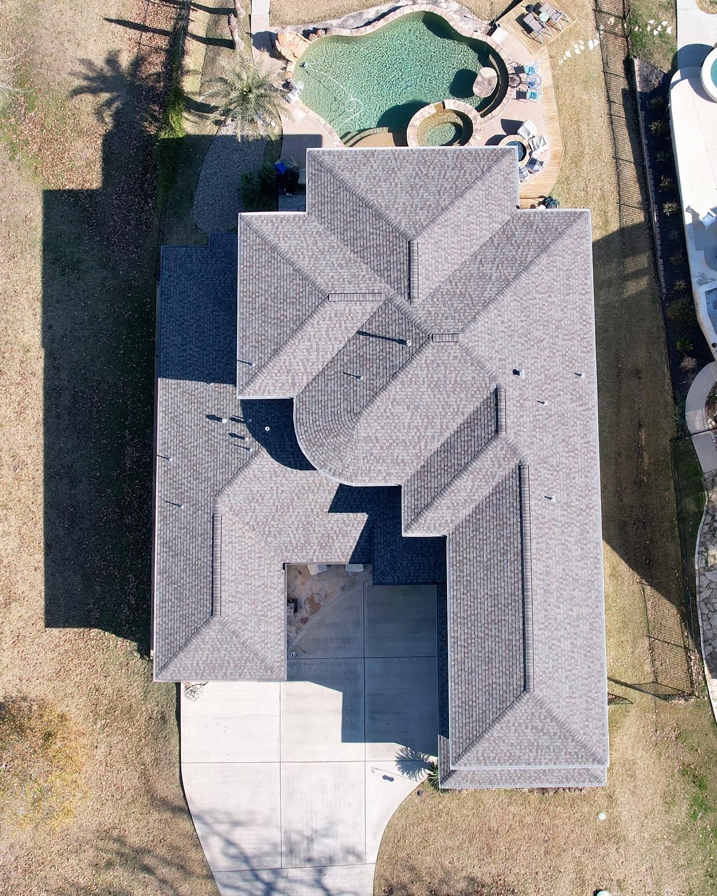 Aerial view of a house with gray shingle roof, concrete driveway, and a backyard pool.