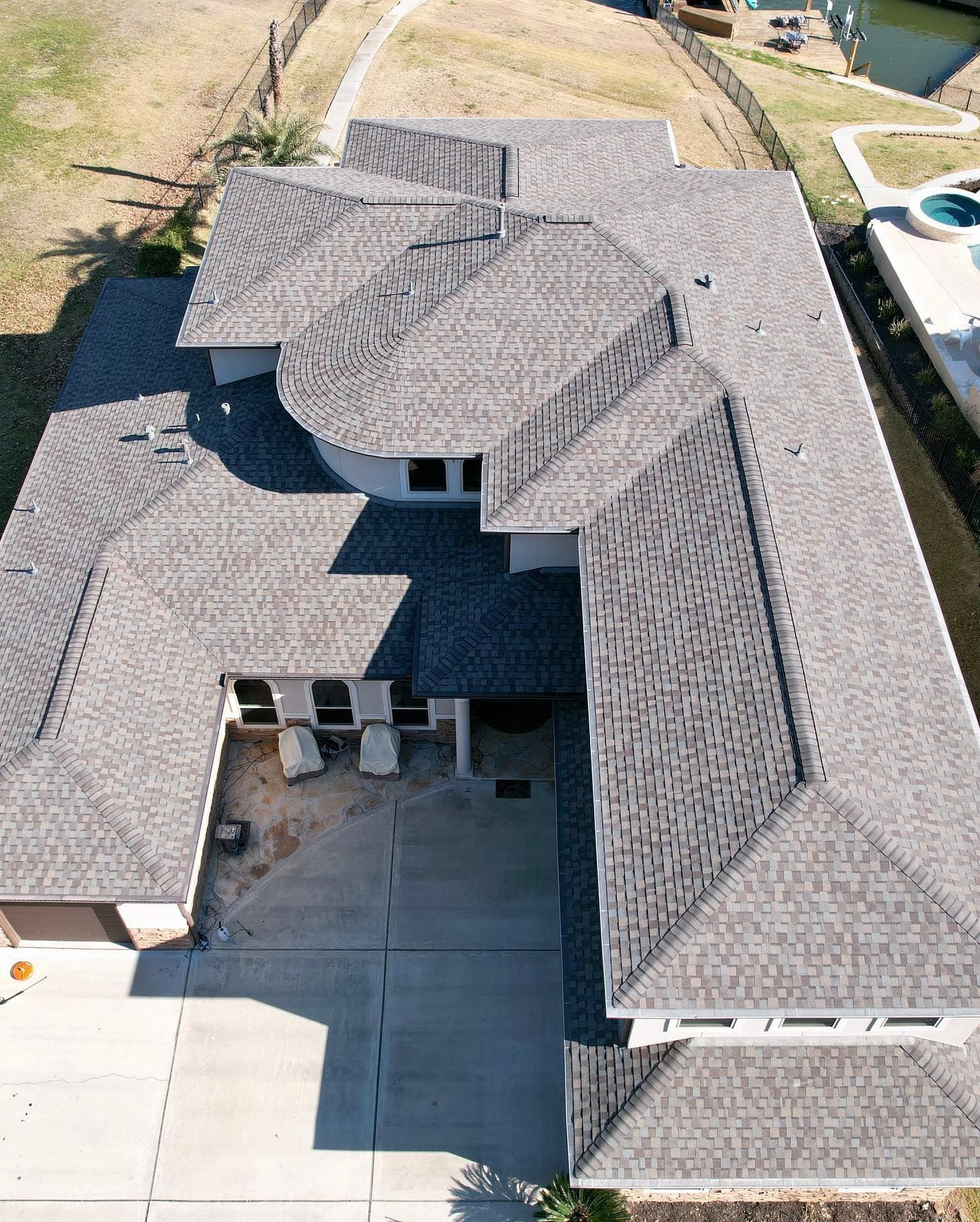 Overhead view of a house with a complex shingle roof, concrete driveway, and a canal.