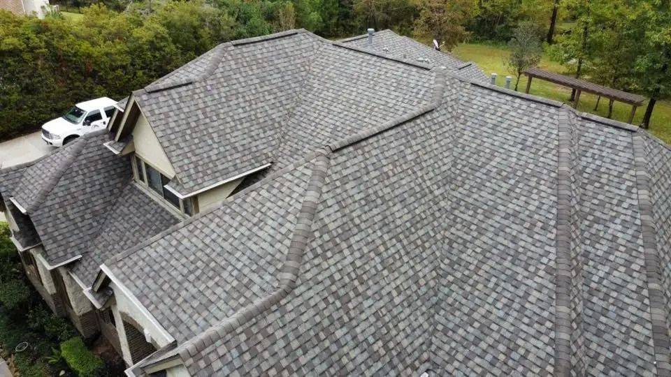 Overhead view of a house with a gray shingle roof, a white vehicle parked, and a green yard.