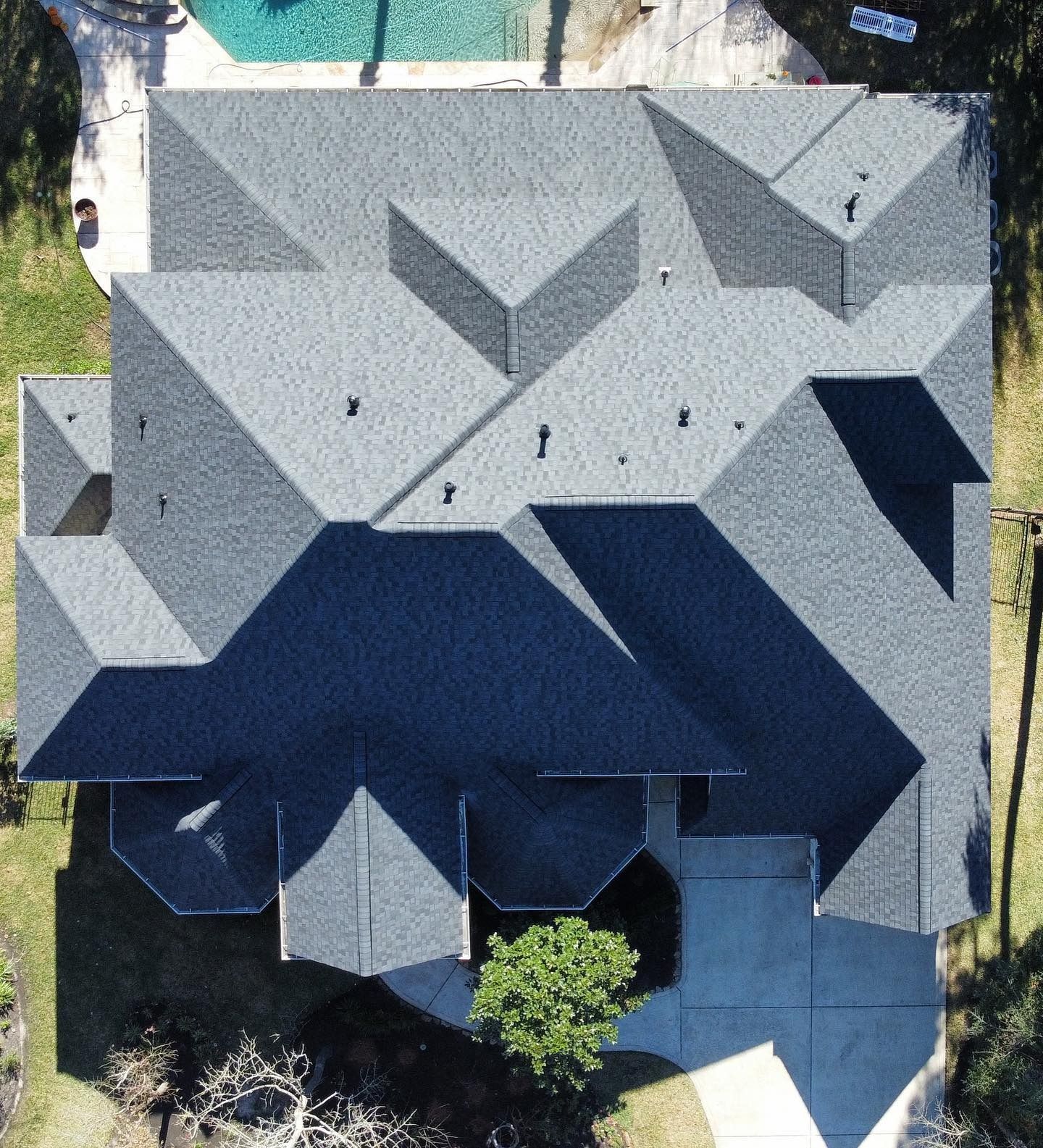 Overhead view of a house with a complex, dark gray roof, a driveway, and a pool.