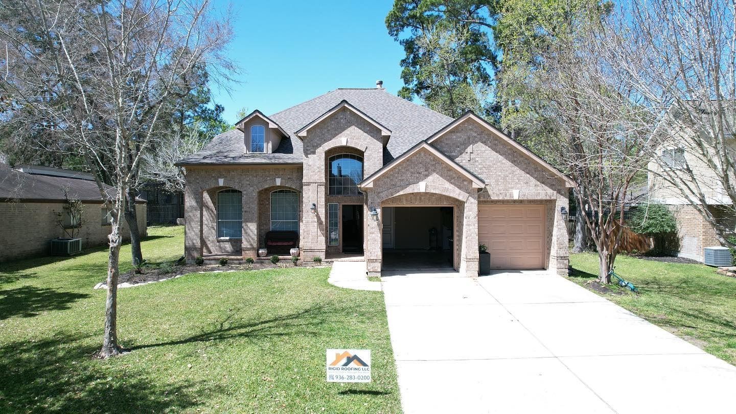 Brick house with a two-car garage, arched entry, and two dormer windows. Green lawn and trees.