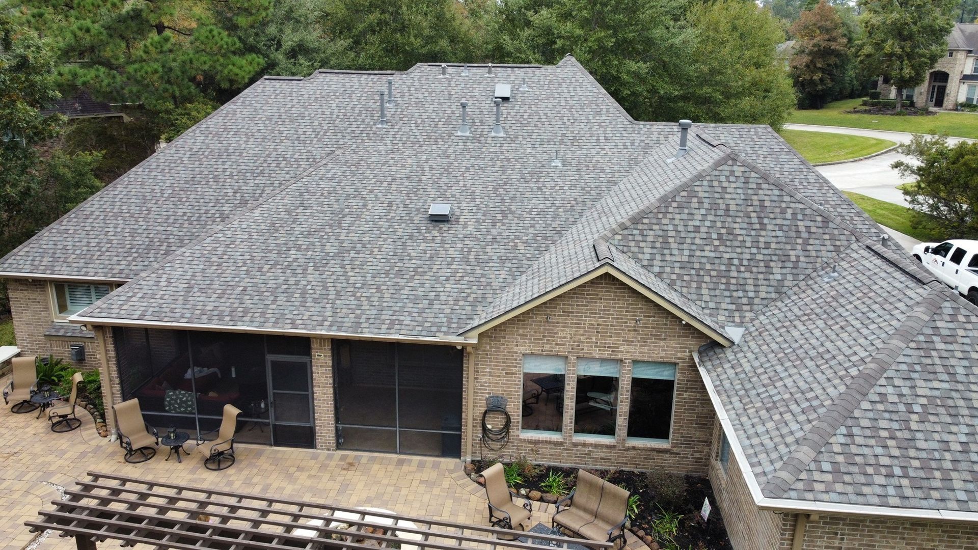 Brick house with a gray shingle roof, screened patio, and a backyard with trees.