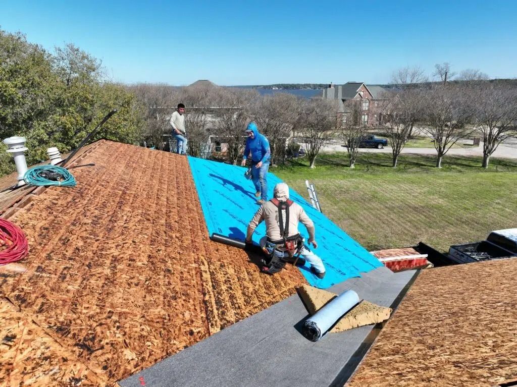 Roofers installing a blue tarp on a roof. Workers on a rooftop, sunny day.