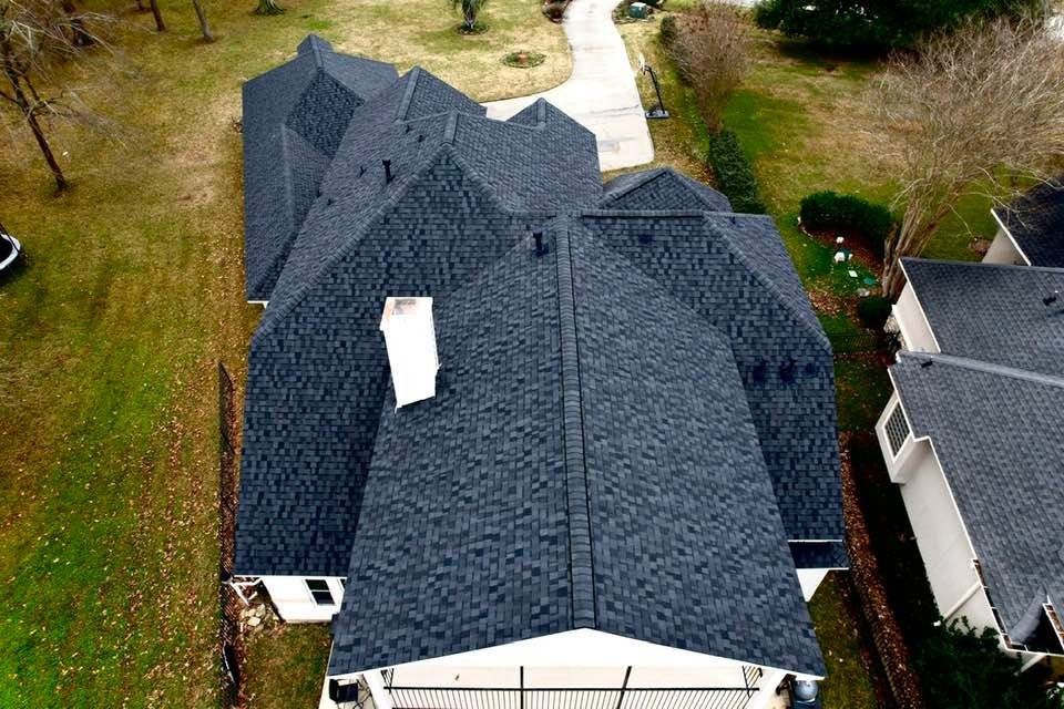 Overhead view of a house with a dark gray shingle roof, chimney, and surrounding green lawn.