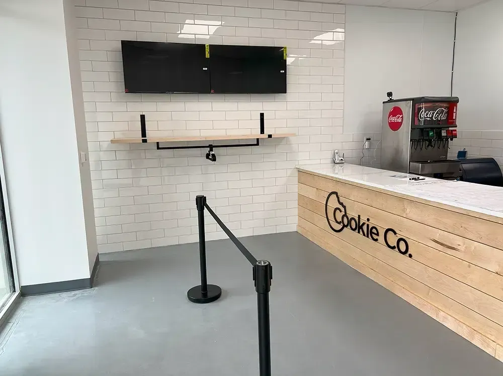 Empty Cookie Co. shop interior with a counter, brick wall, shelves, and a Coca-Cola machine.