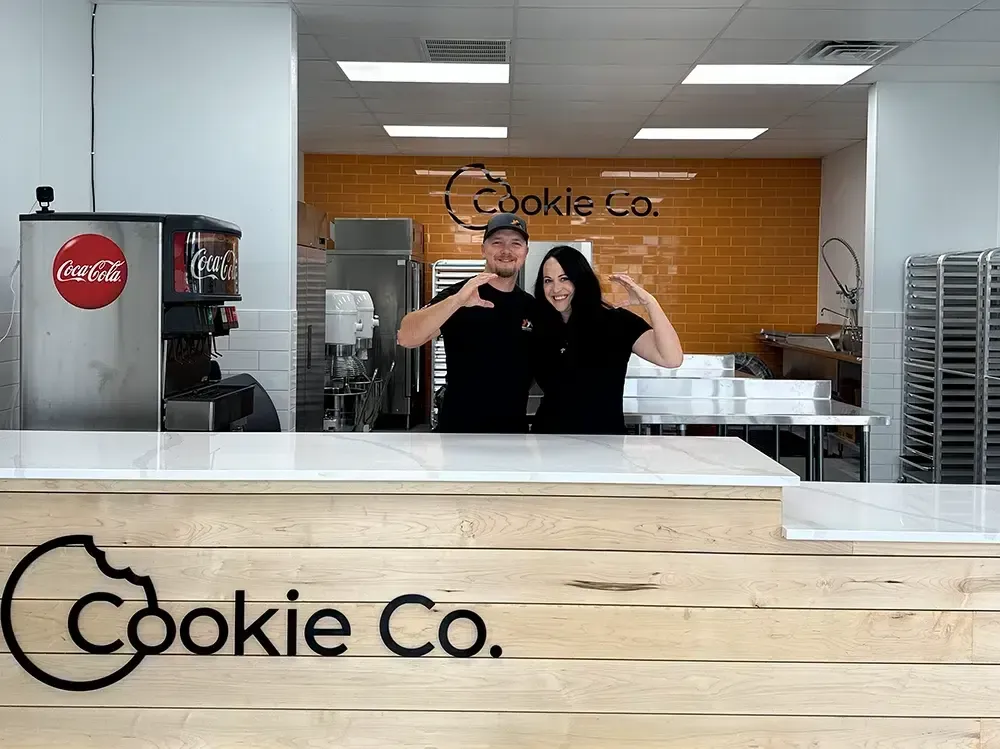 Two people making heart shapes, standing behind a counter with
