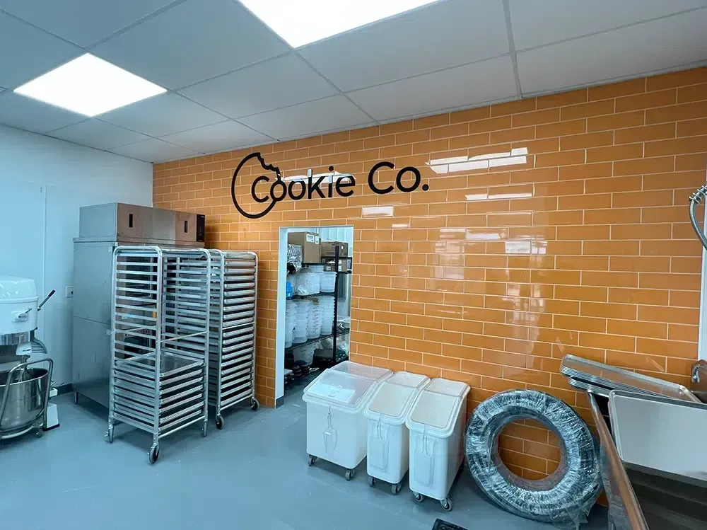 Interior of a Cookie Co. bakery with orange brick wall and stainless steel equipment.