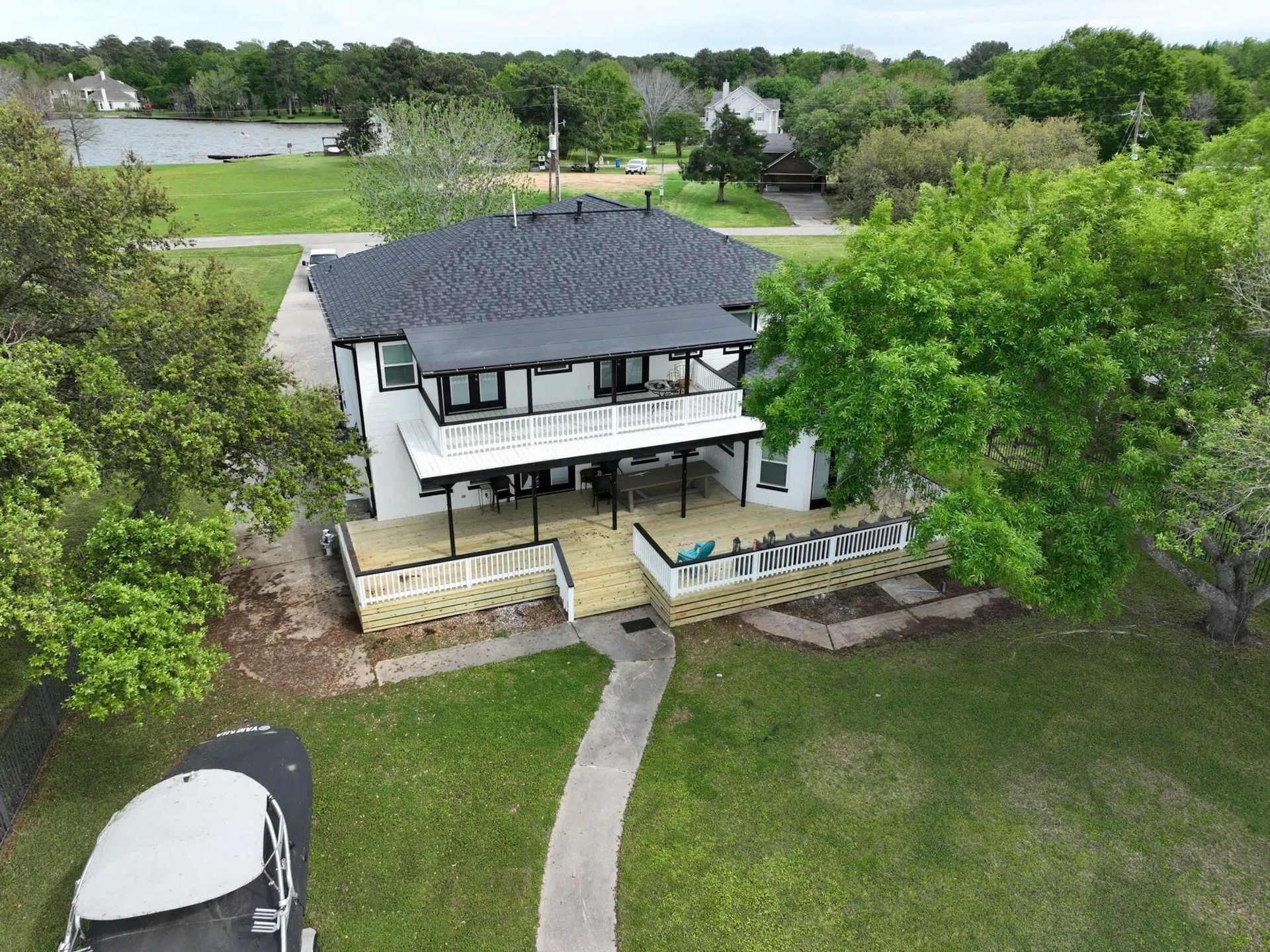Two-story white house with a black roof and deck; surrounded by green grass and trees.