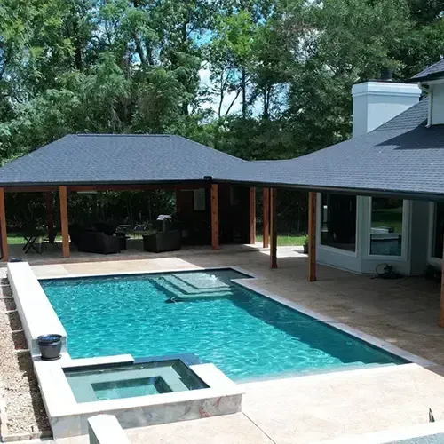 Swimming pool with a connected cabana and the side of a house. Lush green trees are visible in the background.