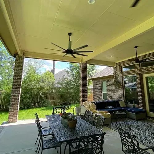 Covered patio with dining table, seating area, ceiling fans, and brick columns.