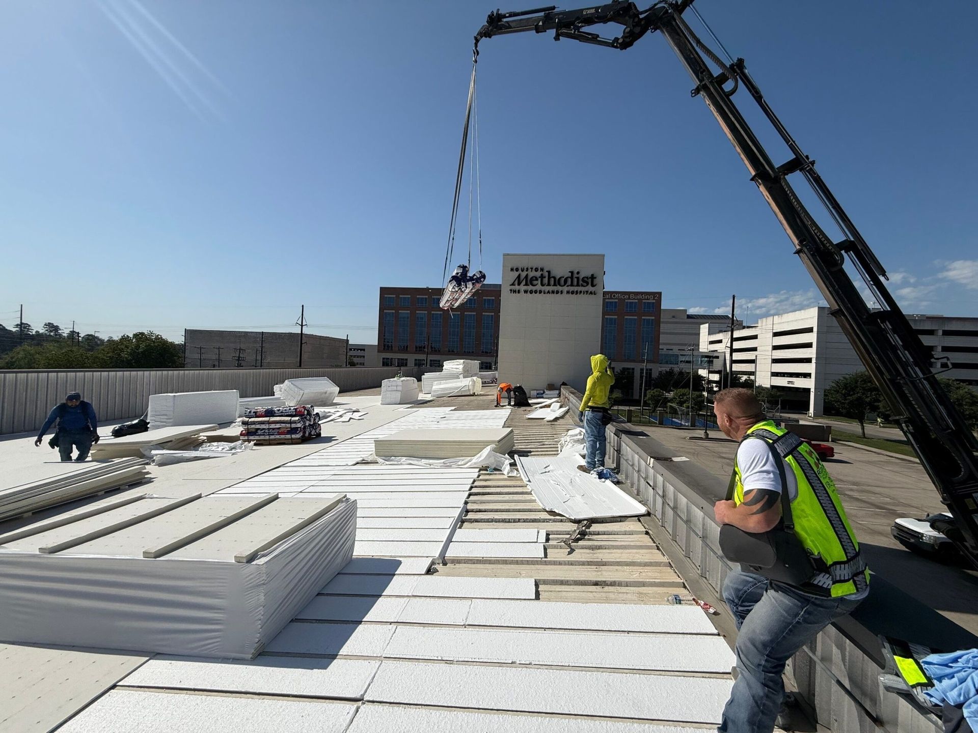 Construction workers installing roofing materials on a flat rooftop with a crane.