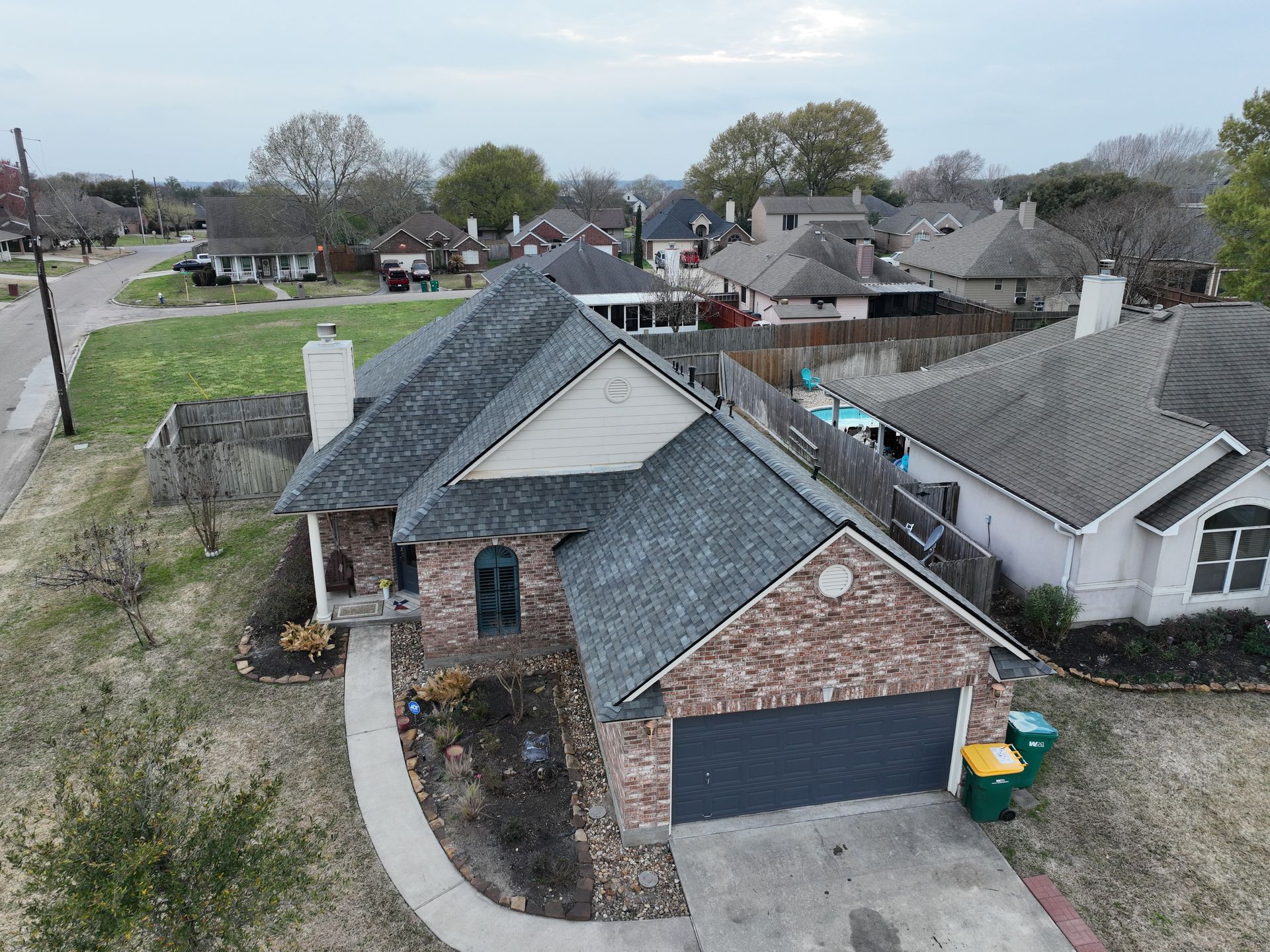 Brick house with gray roof, garage, and yard in a neighborhood.