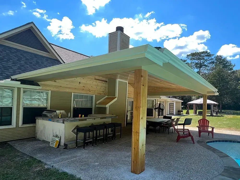Outdoor patio with a bar, dining area, and pool. The patio has a wooden overhang, and a brick chimney.