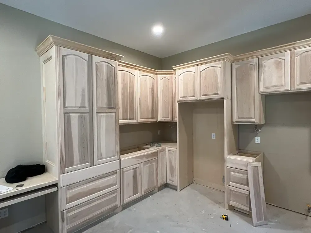 Unfinished light wood kitchen cabinets and desk in a room with light green walls and a concrete floor.