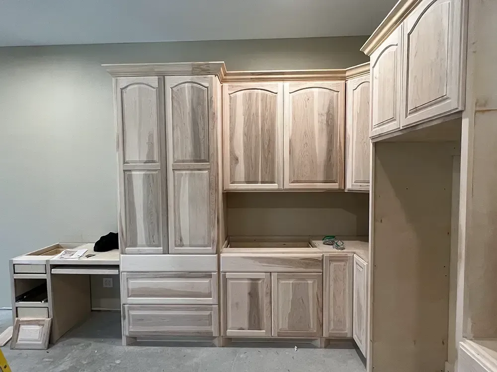 Unfinished light wood kitchen cabinets, some with drawers, near a desk.