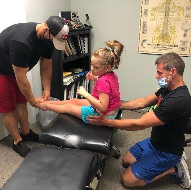 A little girl is sitting on a table with two men kneeling around her.
