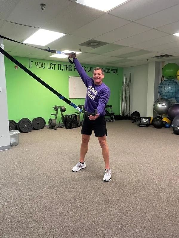 A man in a purple sweatshirt is holding a rope in a gym.