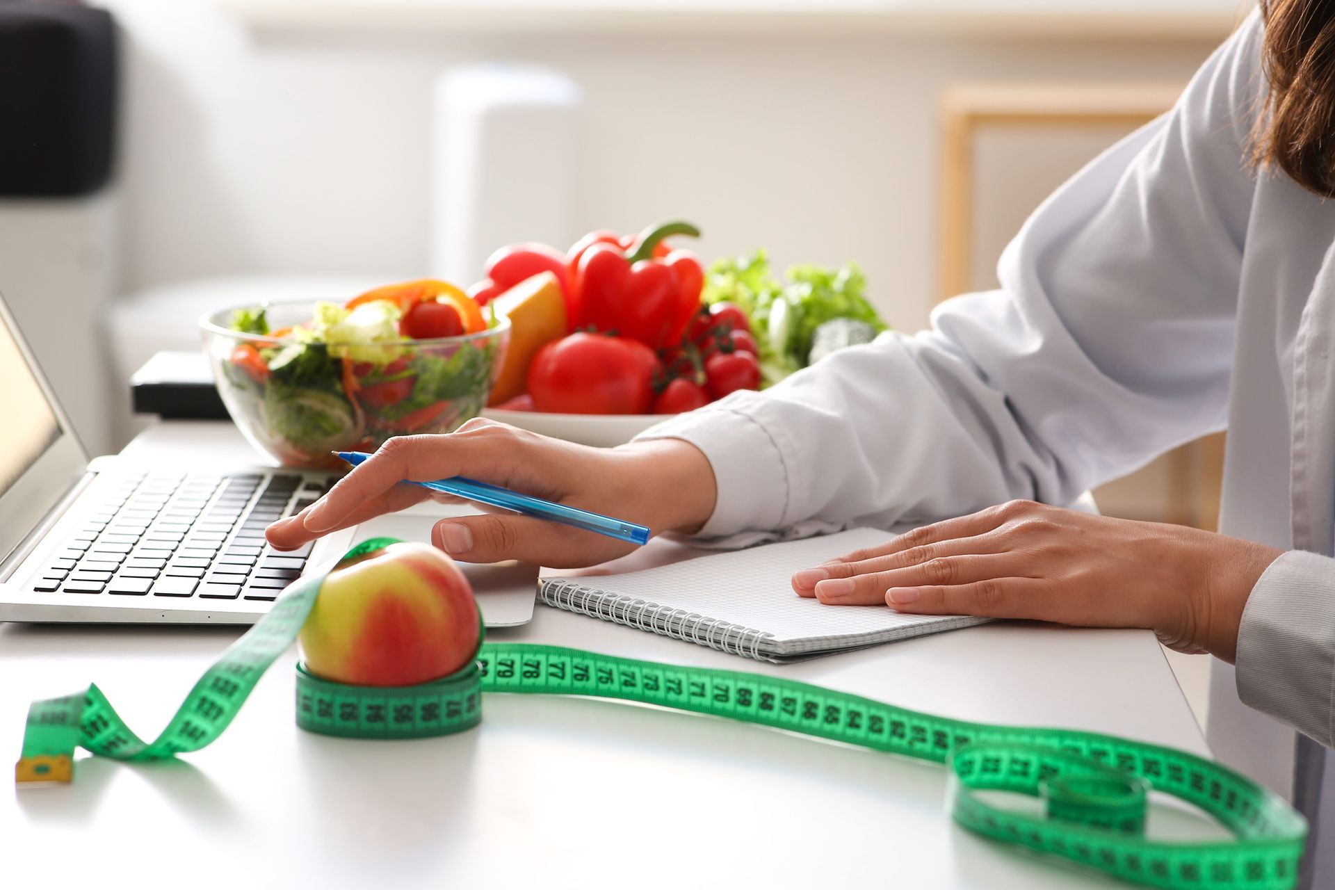 A woman is sitting at a desk with a laptop and a measuring tape.