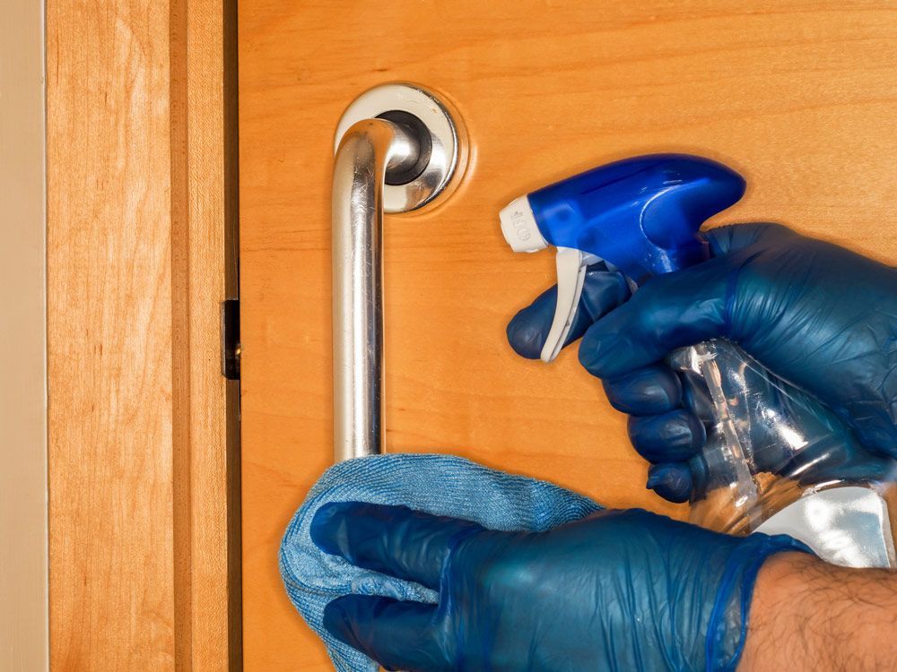 A Person Wearing Blue Gloves Is Cleaning a Door Handle with A Spray Bottle — North Coast Commercial Cleaners In Bli Bli, QLD