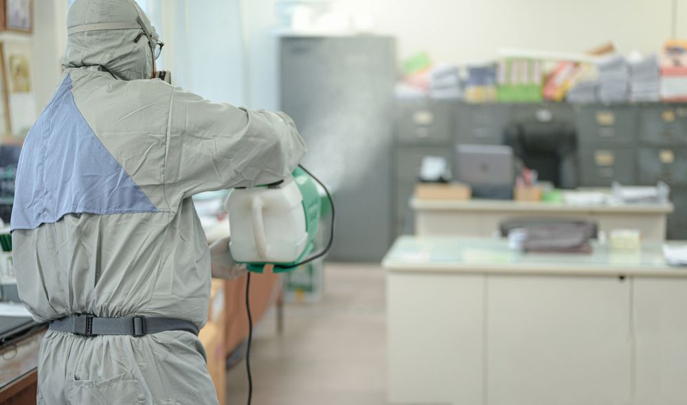 A Man in A Protective Suit Is Spraying Disinfectant in An Office — North Coast Commercial Cleaners In Bli Bli, QLD