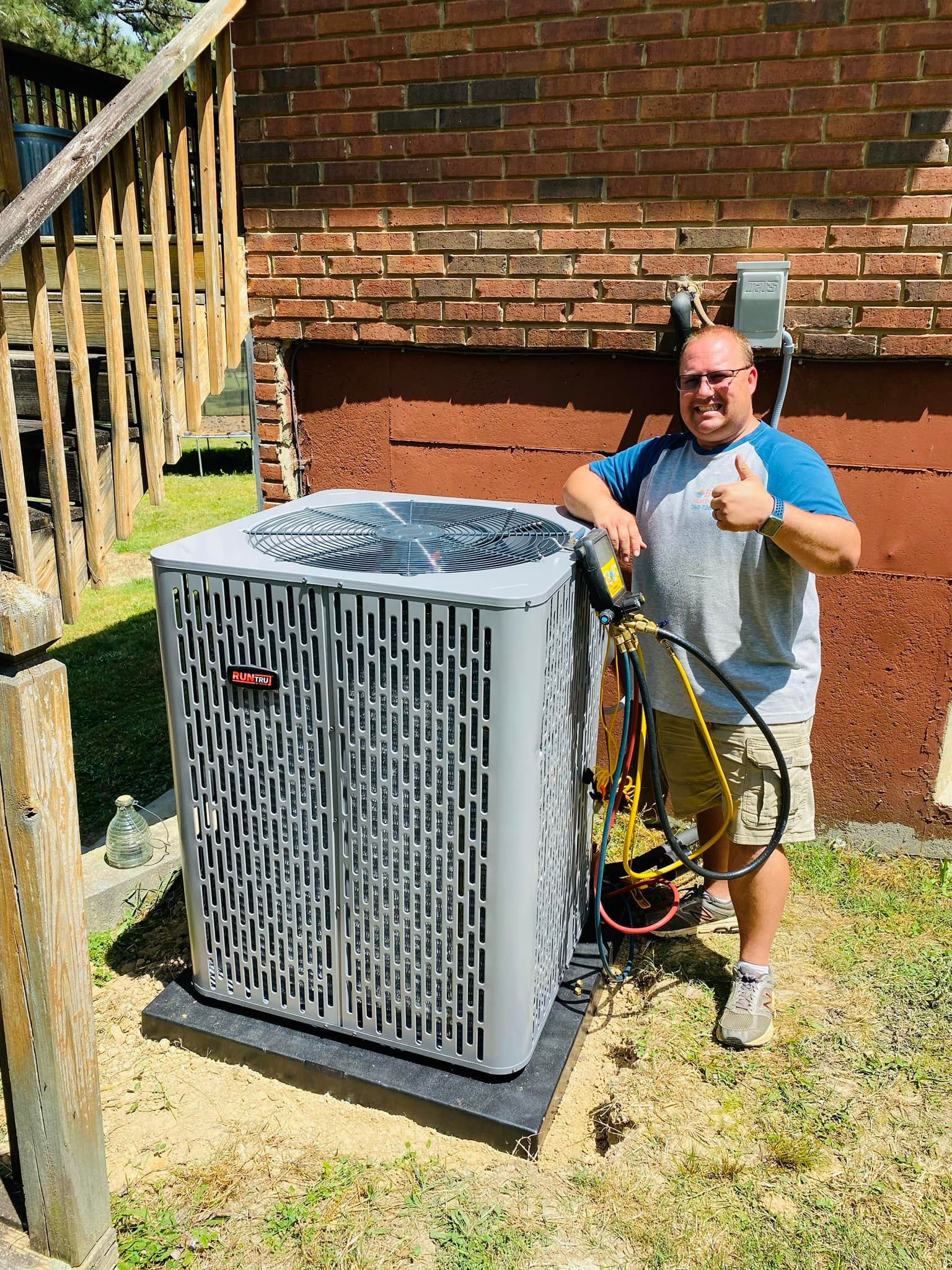 Man giving thumbs up next to new air conditioning unit on a brick building exterior.
