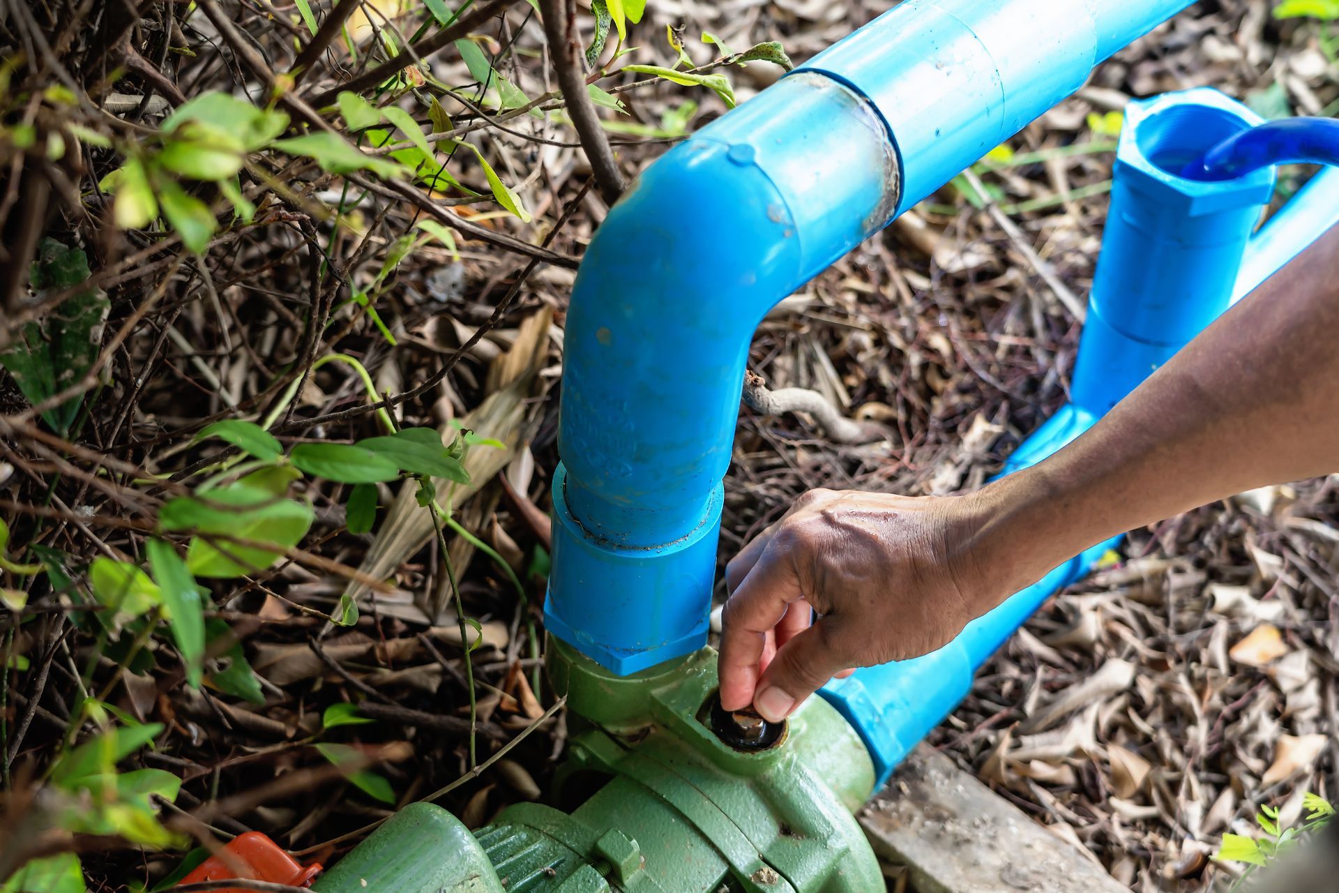 A person is fixing a water pump with a blue pipe.
