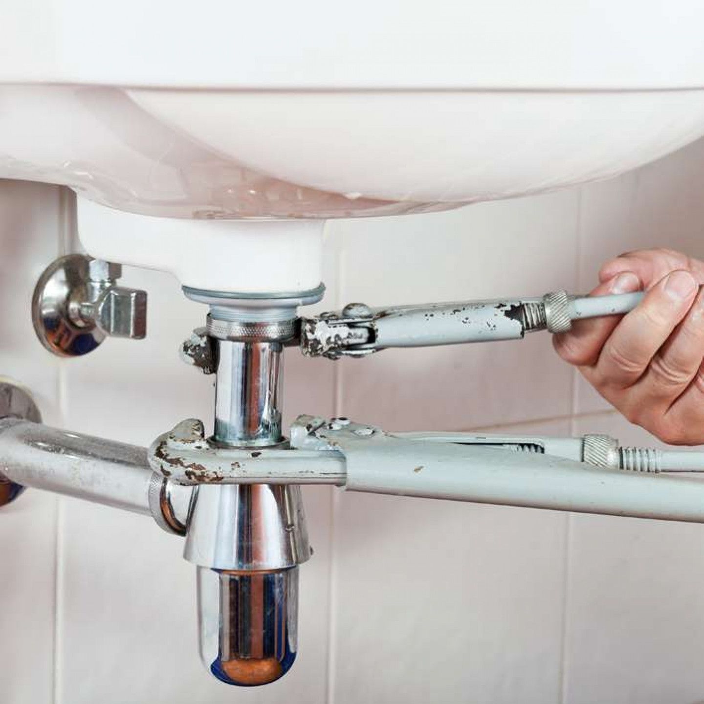 A person is fixing a sink with a wrench.