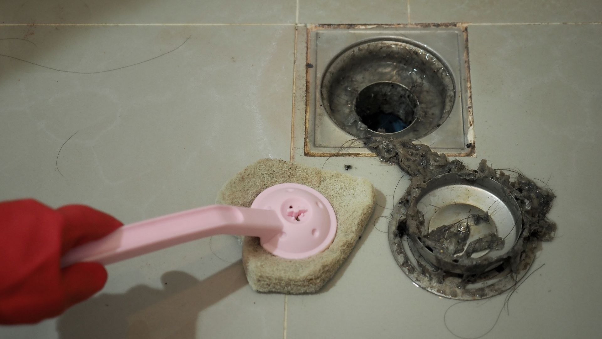 A person is cleaning a drain with a sponge and a brush.