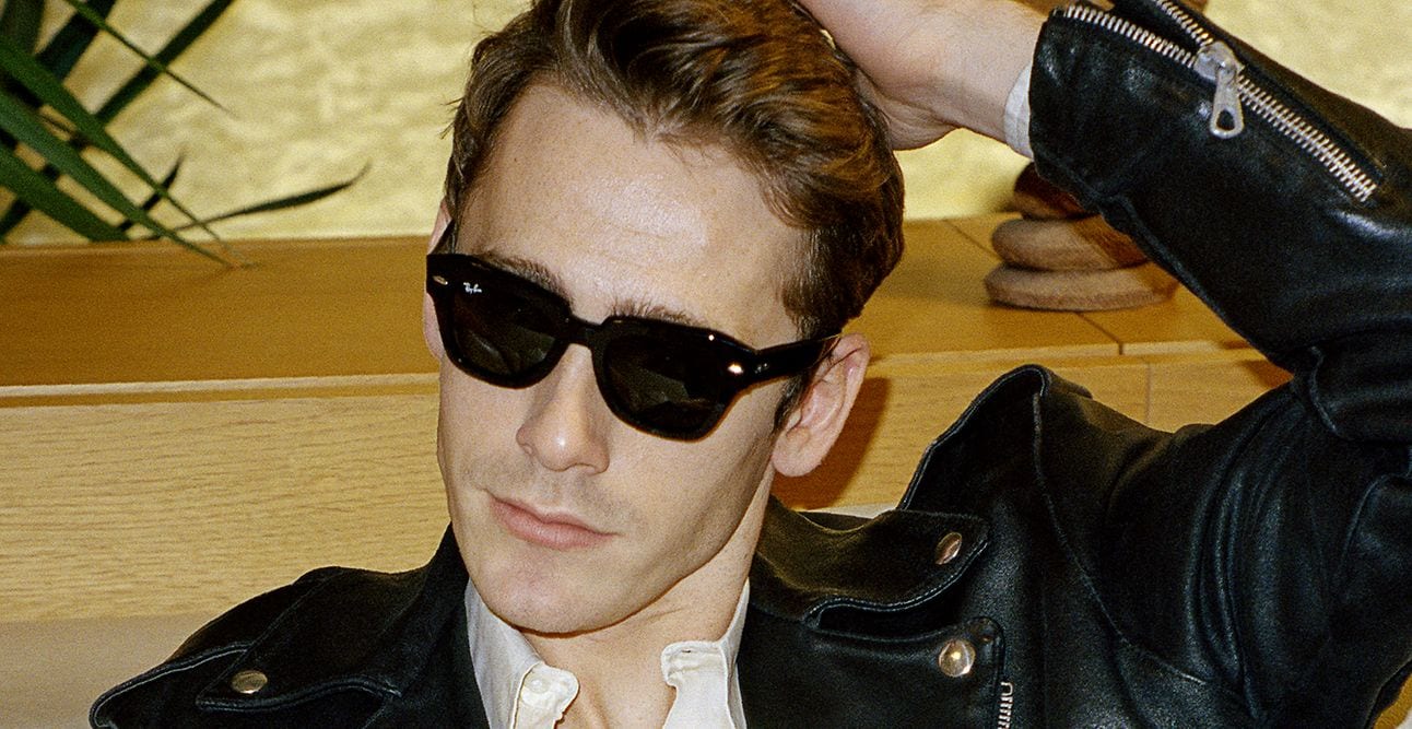 Person in sunglasses and a black leather jacket, leaning back with a hand behind their head.