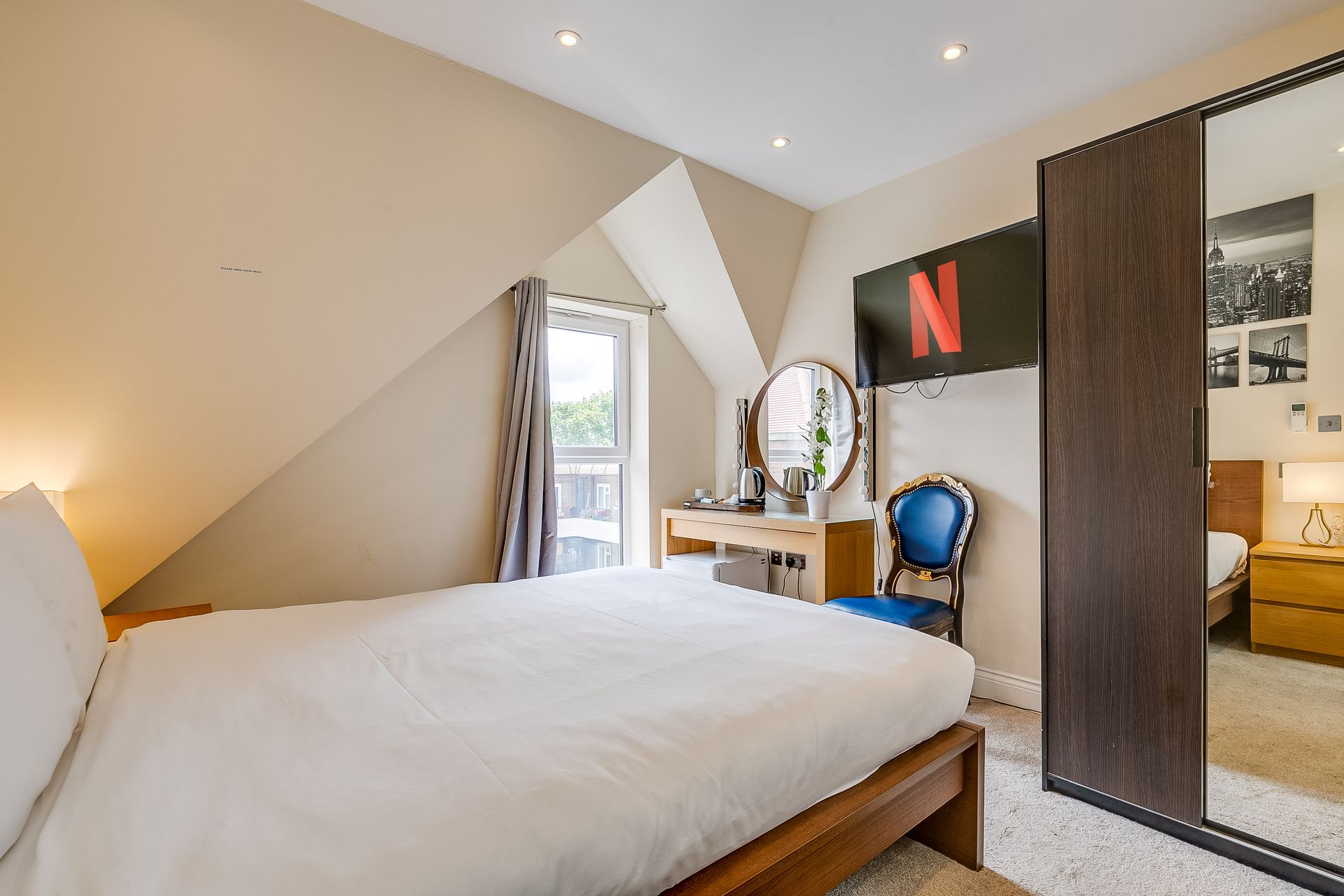 A bedroom with a bed , dresser , mirror and a netflix sign on the wall.