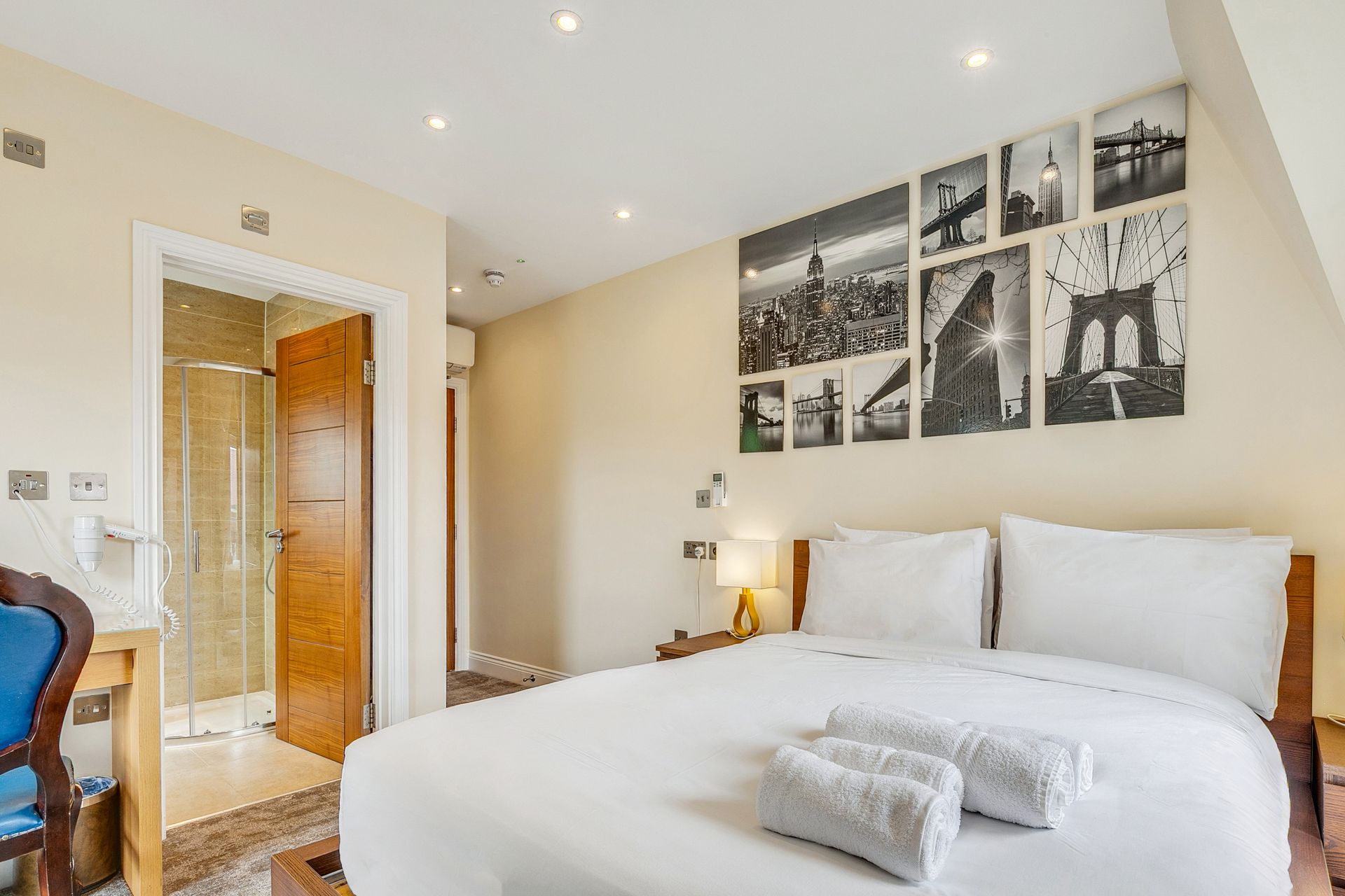 A hotel room with a bed , desk , chair , and paintings on the wall.