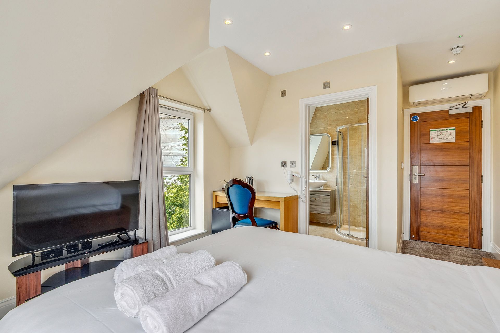 A hotel room with a king size bed , desk , chair and television.