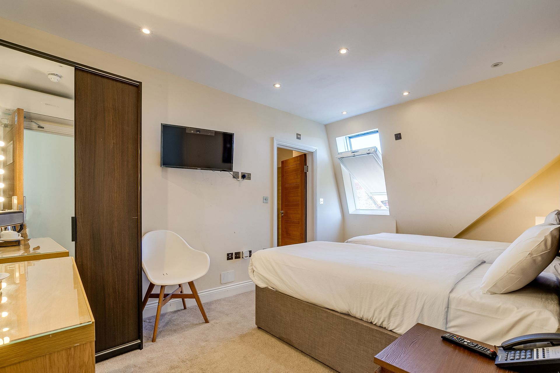 A hotel room with two beds , a chair , a mirror and a flat screen tv.
