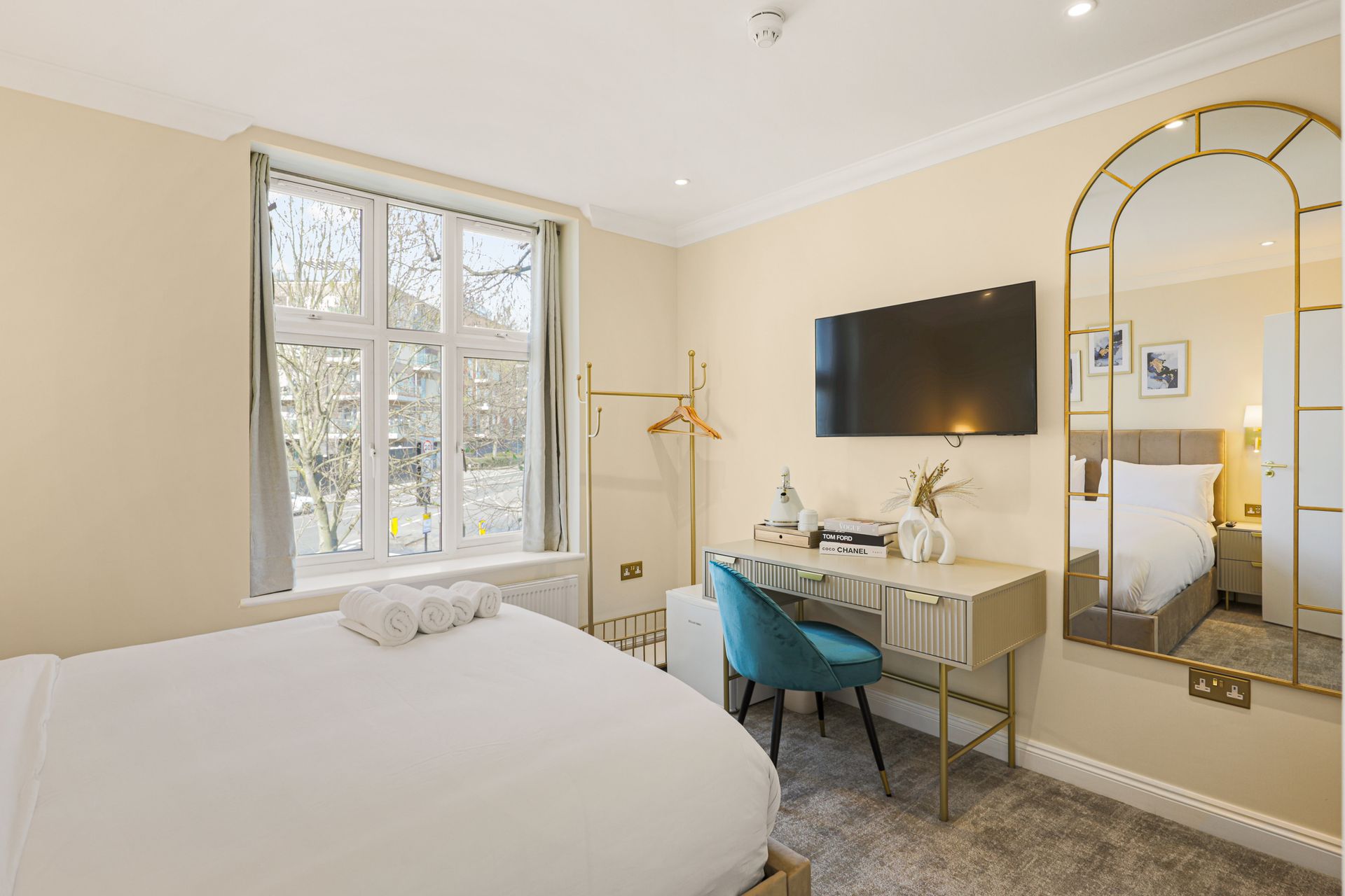 A hotel room with a bed , desk , television and mirror.
