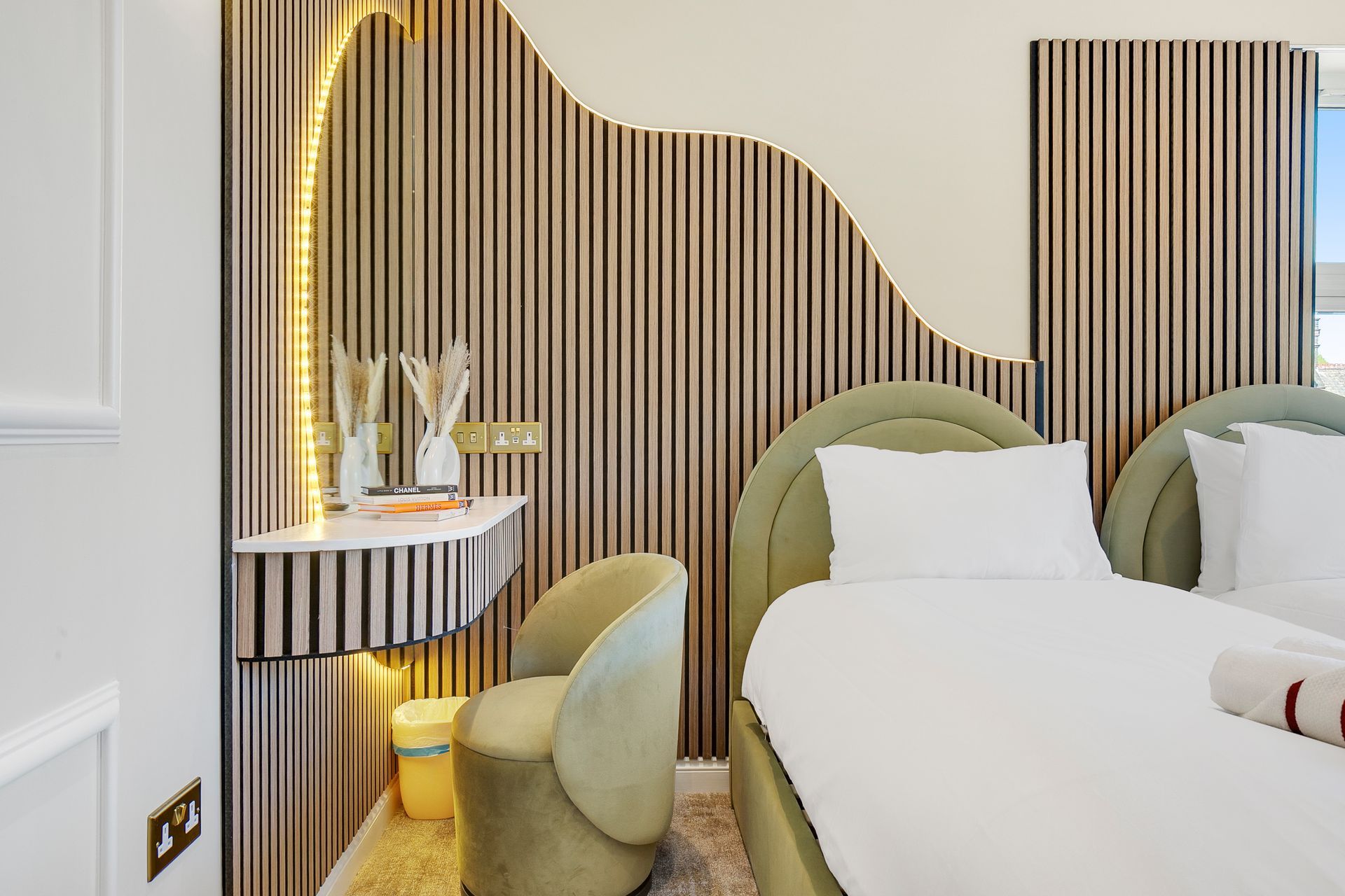 A bedroom with a bed , chair , mirror and striped wallpaper.