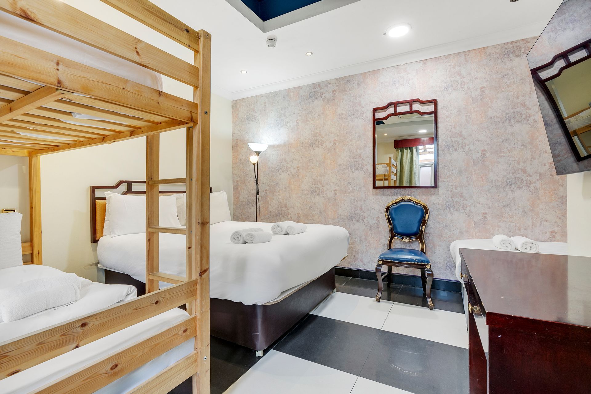 A hotel room with a bunk bed , two beds , a chair and a mirror.