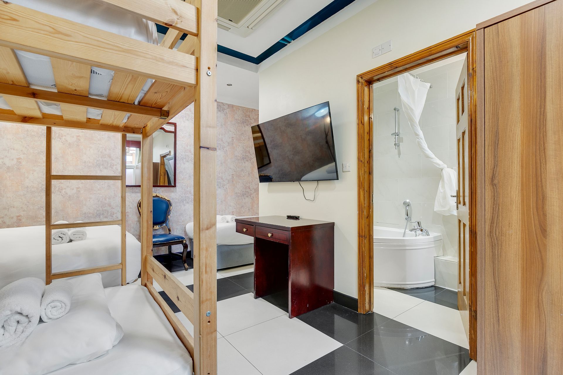 A hotel room with bunk beds , a desk , a television and a bathtub.