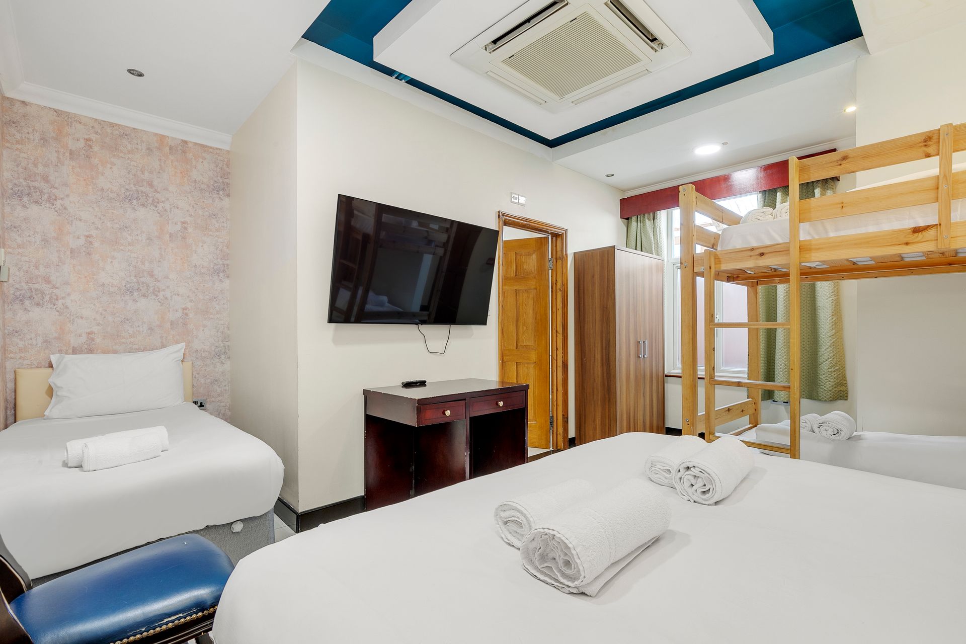 A hotel room with two beds , a bunk bed and a flat screen tv.