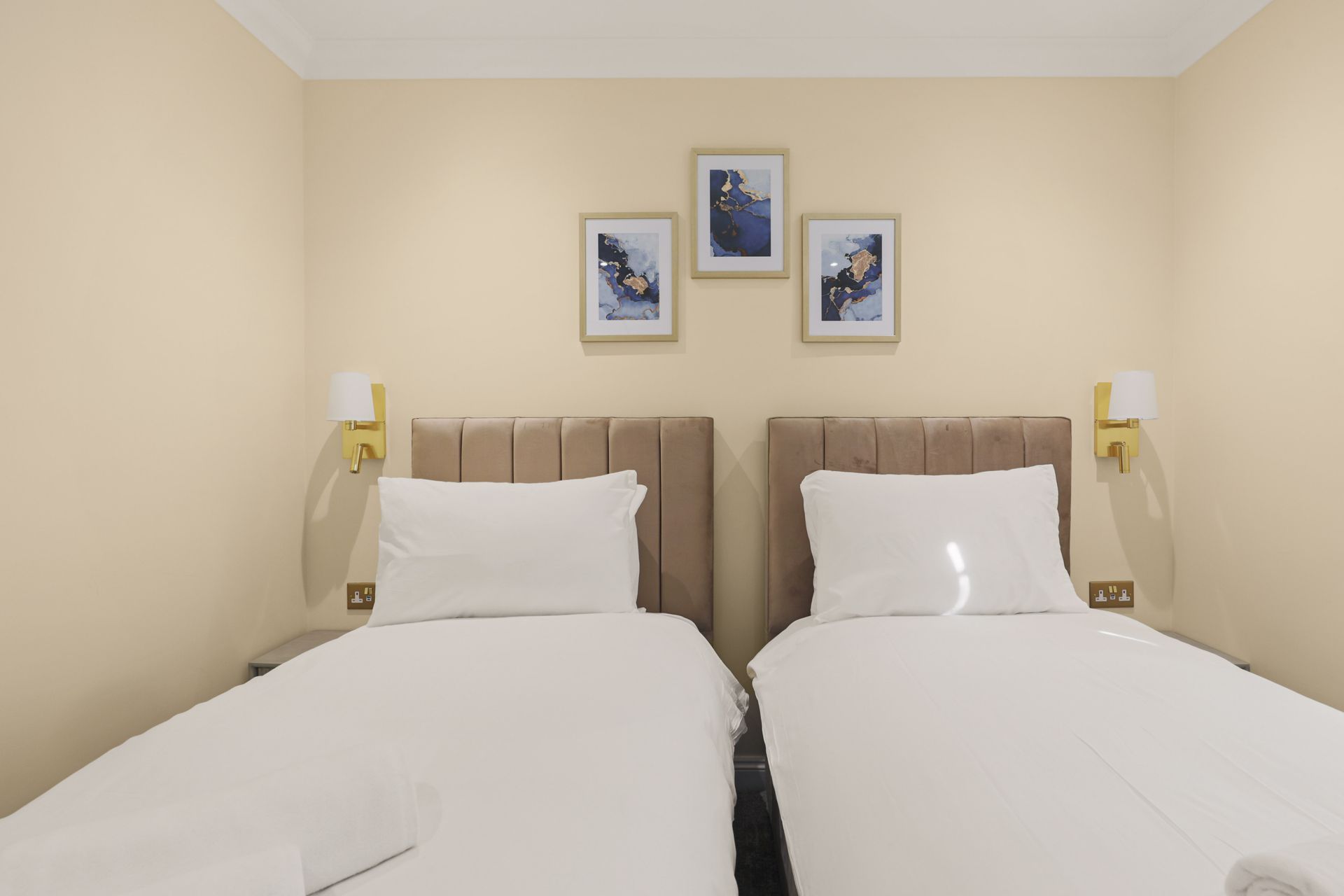 A hotel room with two beds and three pictures on the wall.