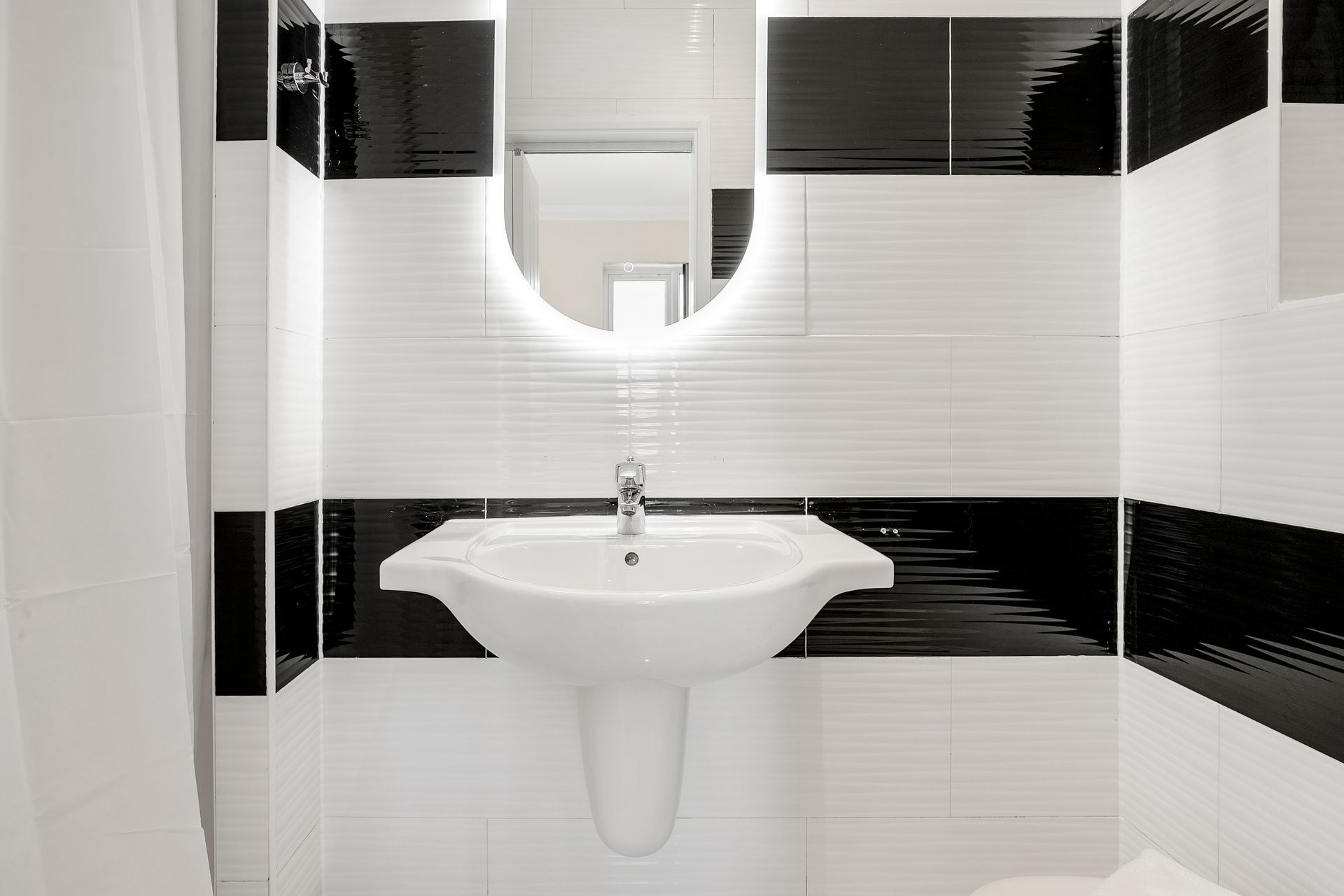 A bathroom with a sink , toilet , mirror and black and white tiles.