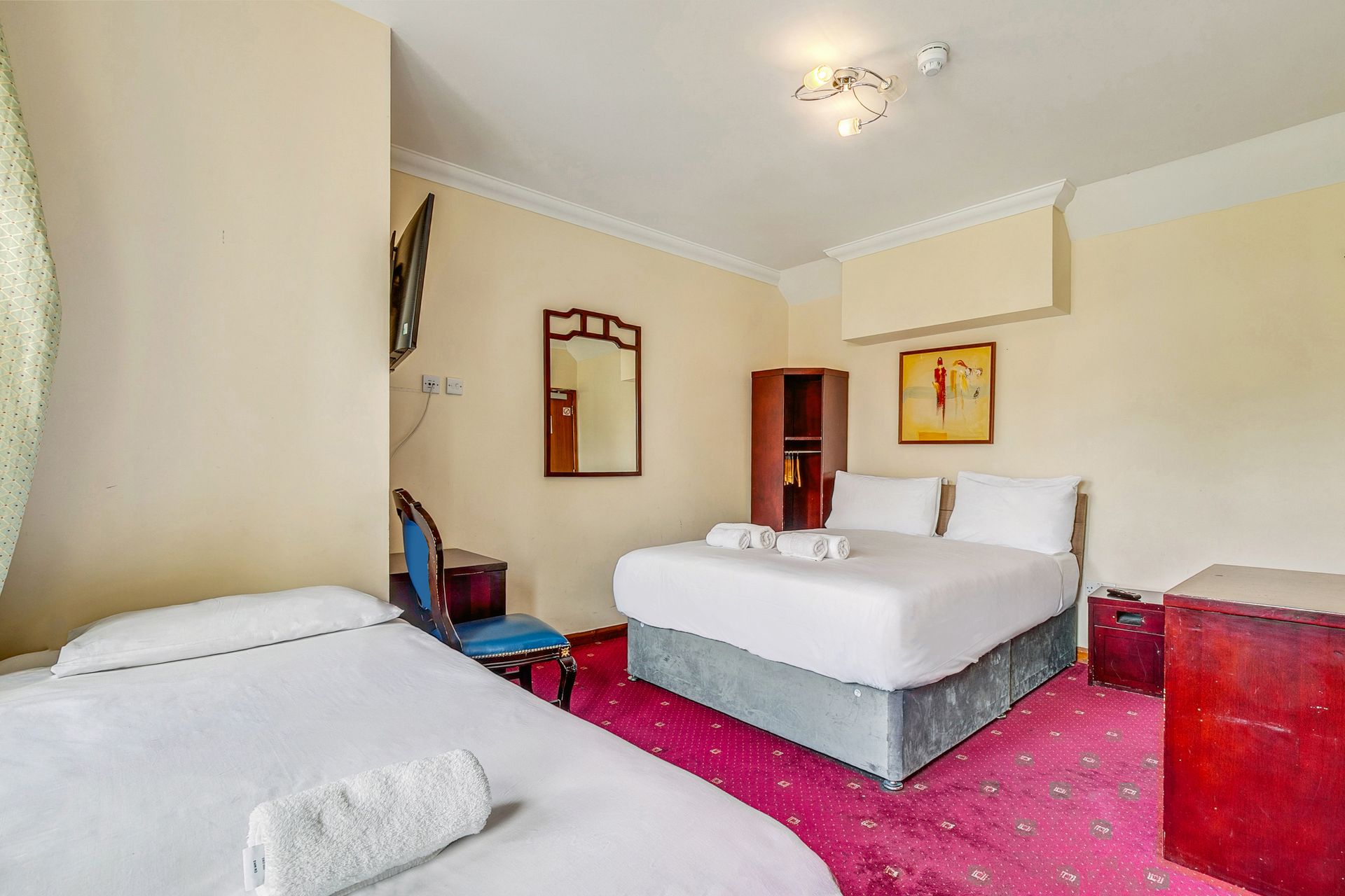A hotel room with two beds , a chair and a mirror.