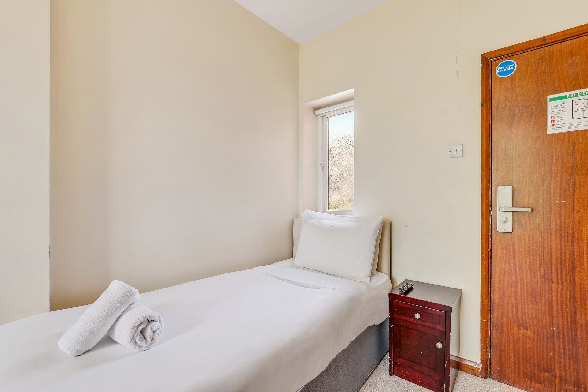 A hotel room with a single bed , nightstand , and window.