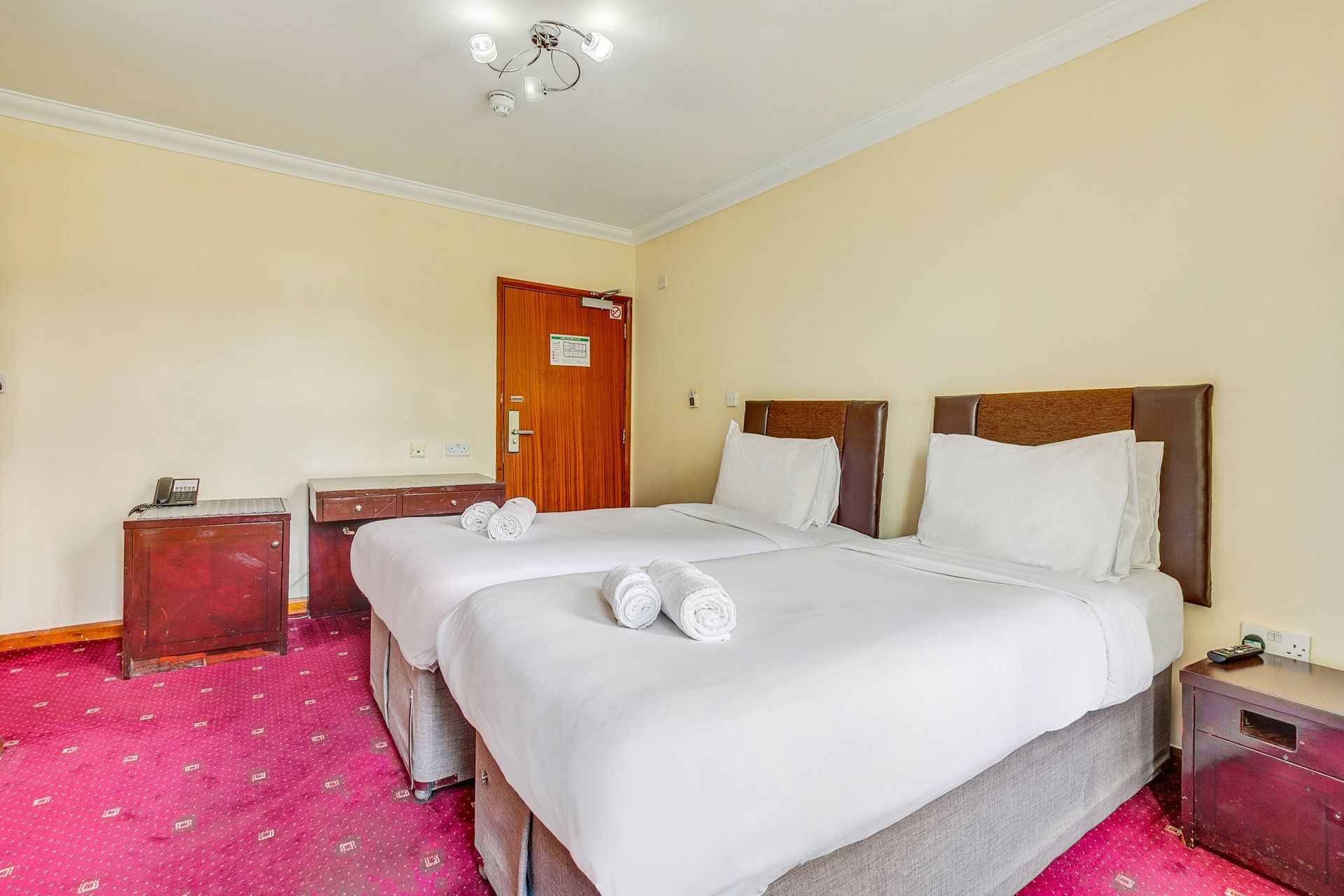 A hotel room with two beds and a pink carpet.