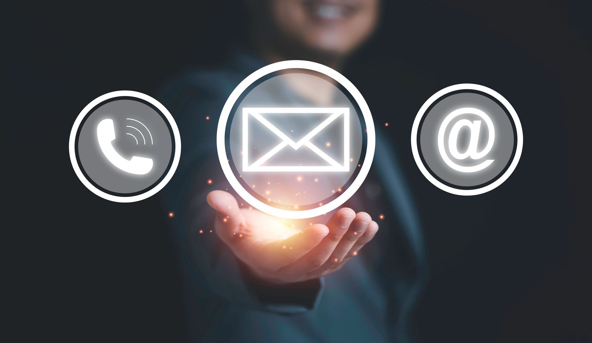 Persona che tiene in mano le icone luminose dei contatti per telefono, email e simbolo @