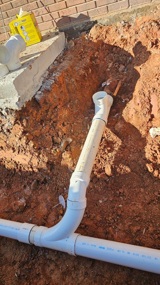 PVC sewer pipe installation in a dirt trench, with a T-joint and vertical vent pipe.