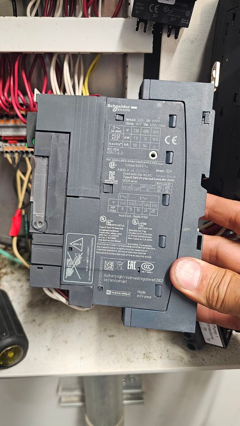 Hand holding a black electrical circuit breaker in an open breaker panel with wires visible