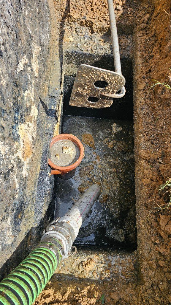 Excavated trench with exposed pipe, green hose, and valve, viewed from above.